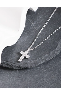 Macro detail of silver cross necklace with sparkling zircons on a textured black stone
