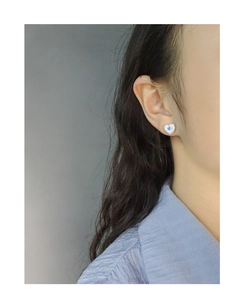 Détail de boucle d'oreille cœur en argent avec zircon bleu et bordure rayée sur le mannequin