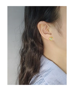 Gros plan d'une boucle d'oreille cœur dorée avec zircon bleu et texture rayée sur modèle