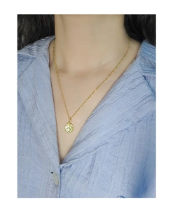 Macro detail of gold round pendant with irregular hammered texture on a fine chain