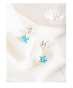 Macro detail of star-shaped gold stud earrings with clear and blue zircon stones