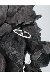 Macro shot of silver twisted rope ring design on textured black charcoal and mirror