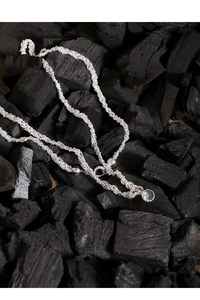 Détail du collier à chaîne tressée argentée avec pendentif cristal rond sur charbon noir