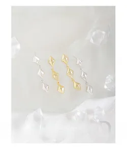 Detail view of triple diamond-shaped drop earrings in polished gold and silver finishes