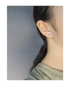 Close-up of minimalist gold star stud earring with blue opal inlay on a female ear lobe