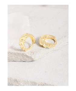 Detailed view of gold twisted croissant huggie earrings on a textured stone surface