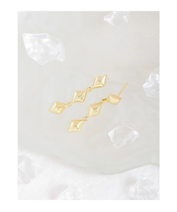 Macro shot of gold geometric rhombus tassel earrings against a crystal ice background