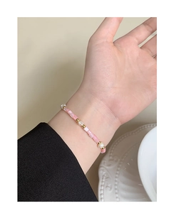 Detailed view of Baroque pearl and pink beaded bracelet on wrist over white ceramic plate