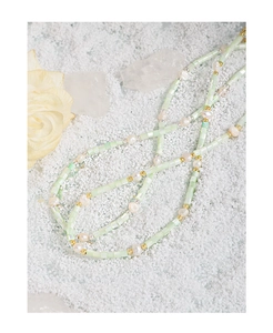 Detail of baroque pearl and light green bead necklace with gold accents on white crystals