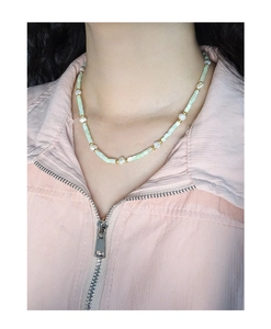 Detail of handcrafted necklace with green beads and baroque pearls on a model's neck