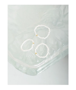 Detailed close-up of three 2mm pearl beaded rings with gold beads on textured glass