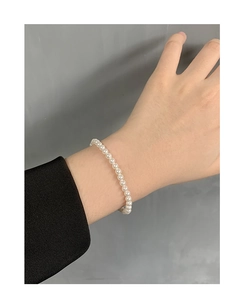 Detail of 4mm-6mm white round pearl bracelet worn on wrist with black sleeve contrast