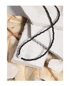 Detailed shot of black bead necklace with a white opal-like center stone on stone backdrop