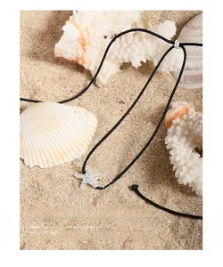 Detail of S925 silver starfish pendant on black cord over sand and seashells