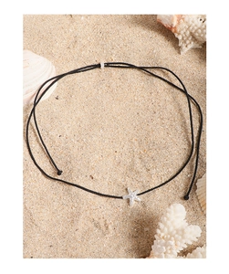 Detail view of adjustable black cord necklace with silver starfish pendant on beach sand