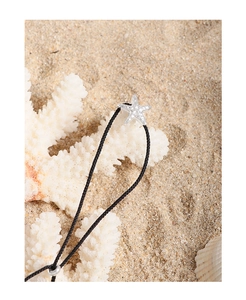 Detailed view of S925 sterling silver starfish pendant on black cord over beach sand
