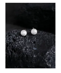Macro view of matte brushed silver ball earrings on a textured volcanic rock background