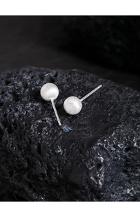 Detailed macro view of matte brushed silver ball stud earrings on black volcanic rock