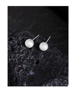Macro detail of matte brushed silver ball earrings on a textured dark stone background