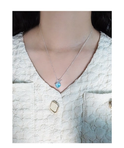 Detail of S925 silver necklace with blue heart-shaped pendant on a female model