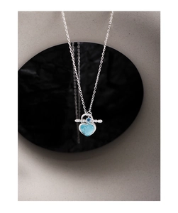 Macro detail of S925 silver heart necklace with blue gems on a grey stone display
