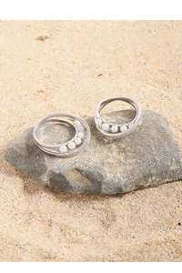 Close-up of silver-tone crisscross rings with white pearls and small zircon on a rock
