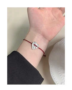 Detail of red braided drawstring bracelet with textured S925 silver heart charm on wrist