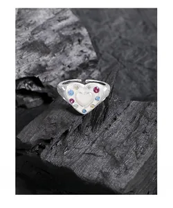 Macro detail of S925 silver heart ring featuring colorful zircons on a dark stone background
