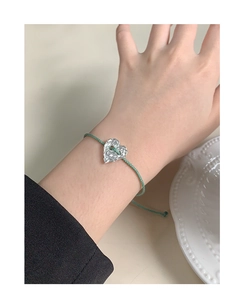 Detail of silver heart bracelet with hammered texture on a green braided cord strap