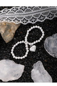 Gros plan d'un bracelet en argent S925 perlé avec pendentif cœur sur pierres noires