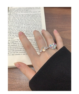 Close-up of S925 silver heart ring with colorful zircon stones worn over a book