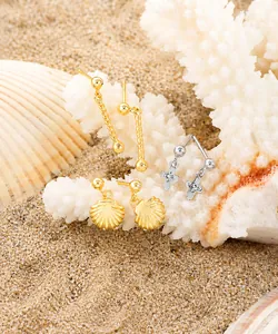Detailed shot of shell cross earrings and spiral gold studs on white sand coral