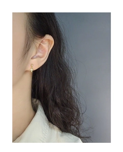 Detailed view of a gold shell cross stud earring with sparkling zircon inlays on ear