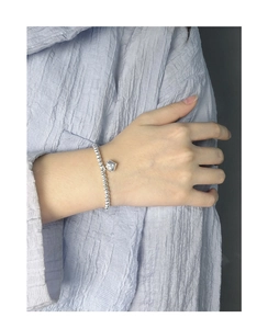 Gros plan d'un bracelet perlé en argent S925 avec pendentif cœur au poignet du modèle