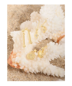Detailed view of three pairs of gold stud earrings featuring shells and crosses on sand