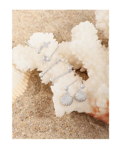 Three pairs of silver S925 cross and shell earrings displayed on white coral over sand