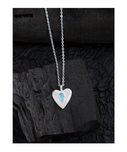 Macro shot of silver heart pendant with light blue teardrop crystal on black wood