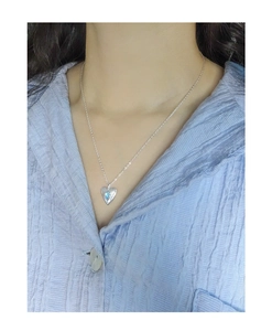 Close-up of S925 silver heart necklace with blue crystal on model neck with blue shirt