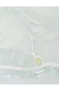 Detail of S925 silver necklace featuring an oval green crystal on textured glass