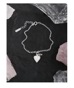 Detail of S925 sterling silver heart bracelet with pink bead on a dark stone background