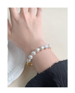 Bracelet en perles baroques avec fermoir OT doré porté au poignet sur assiette en céramique
