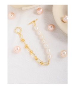 Détail du collier de perles baroques et chaîne dorée avec fermoir OT sur tissu