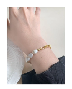 Gros plan d'un bracelet en perles baroques et maillons dorés sur un poignet féminin élégant