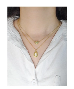 Gros plan du collier double doré avec pendentif cœur et pierre œil de chat blanche