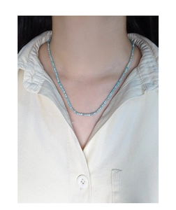 Detail van turquoise kralenketting op linnen overhemd met gefacetteerde textuur look