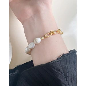 Élégant bracelet en perles baroques et chaîne dorée porté au poignet pour femme en argent