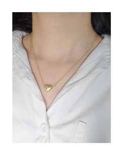 Gros plan d'un collier avec pendentif cœur 3D doré sur un mannequin en chemise blanche