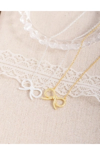 Close-up of gold and silver hollow bow necklaces on a textured fabric and lace background