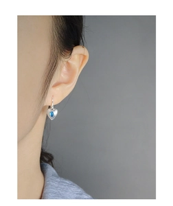 Detail of heart-shaped silver earrings with blue teardrop gemstone on female model