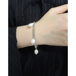 Baroque pearl bracelet on silver metal chain worn by a model against dark background